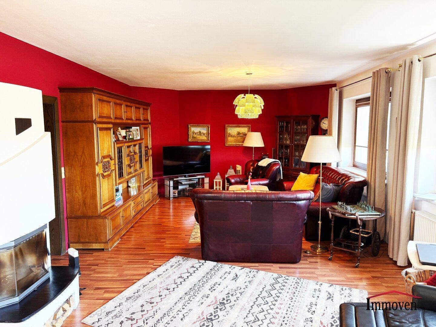 Geräumiges Wohnzimmer mit roter Akzentwand, Ledersofas und Holzparkettboden.