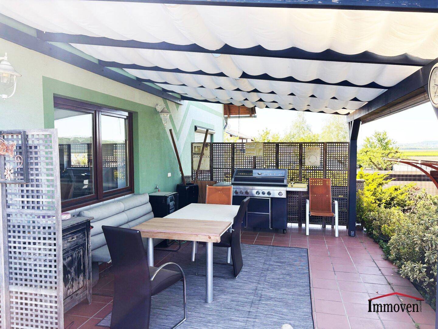 Überdachte Terrasse mit Grillbereich, Esstisch und Blick ins Grüne.