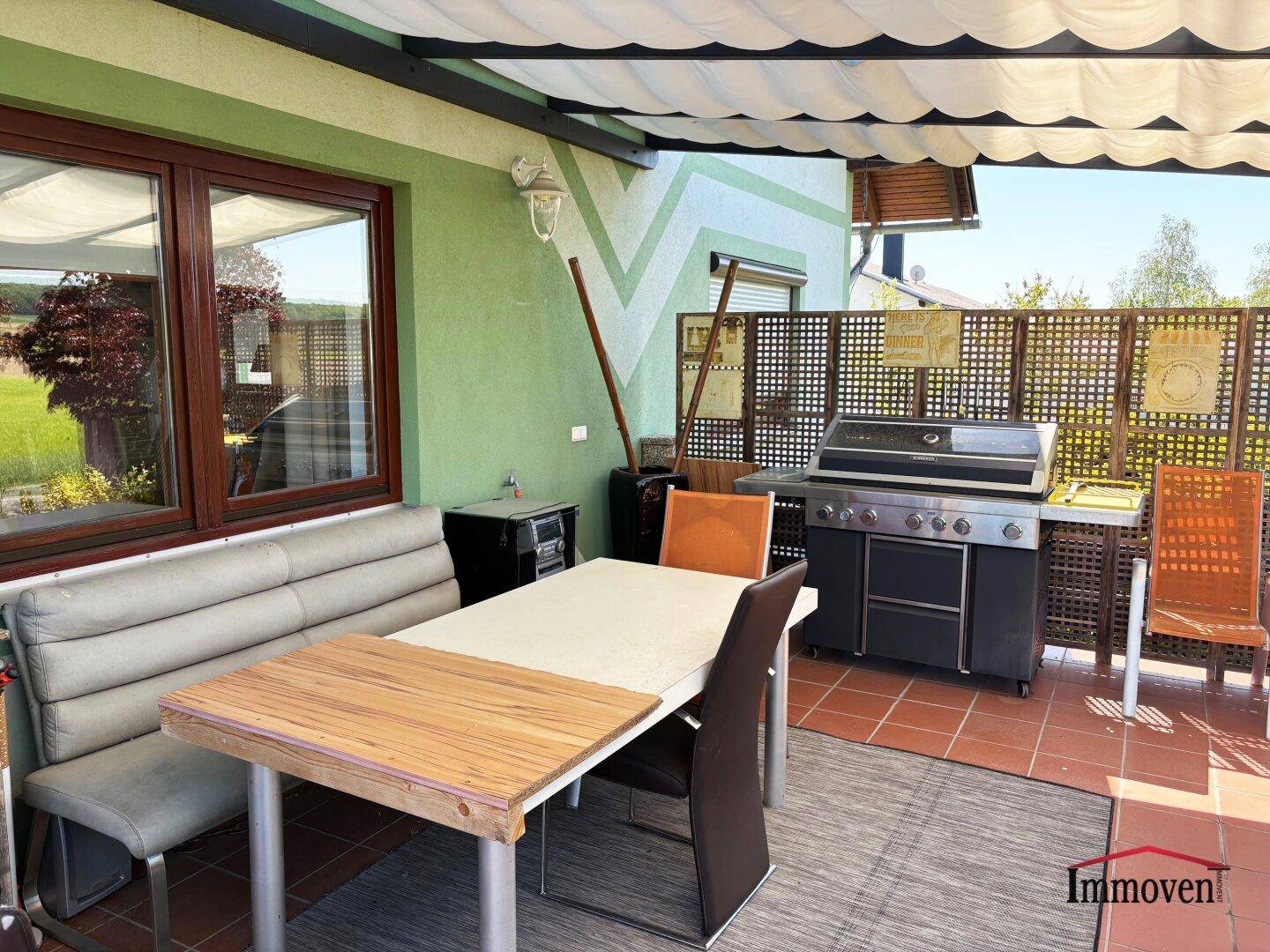 Gemütlicher Essbereich auf der überdachten Terrasse mit Grill und Gartenblick.