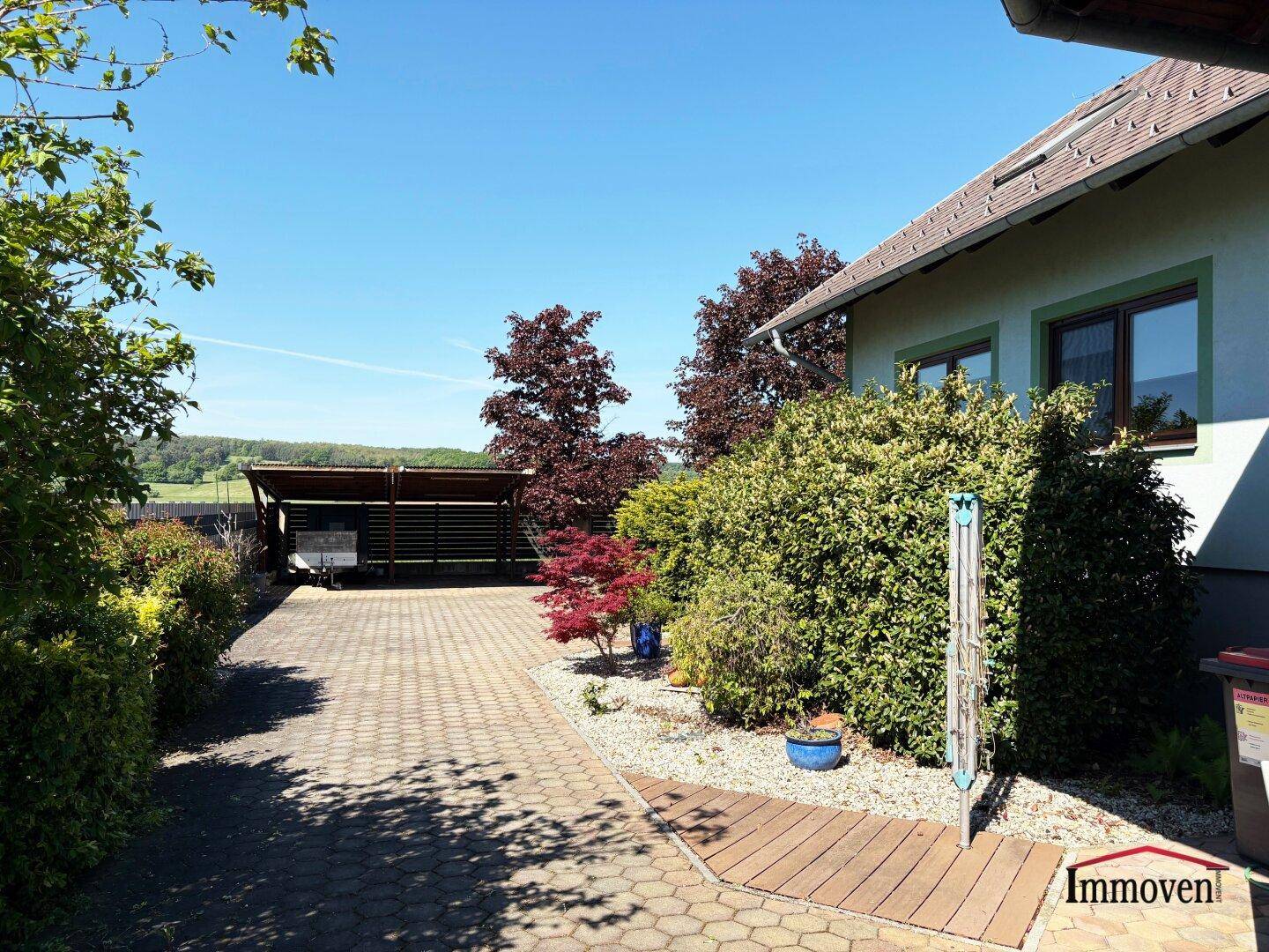 Vorgarten und Auffahrt mit Landschaftsgestaltung, Carport im Hintergrund und Hausfassade.