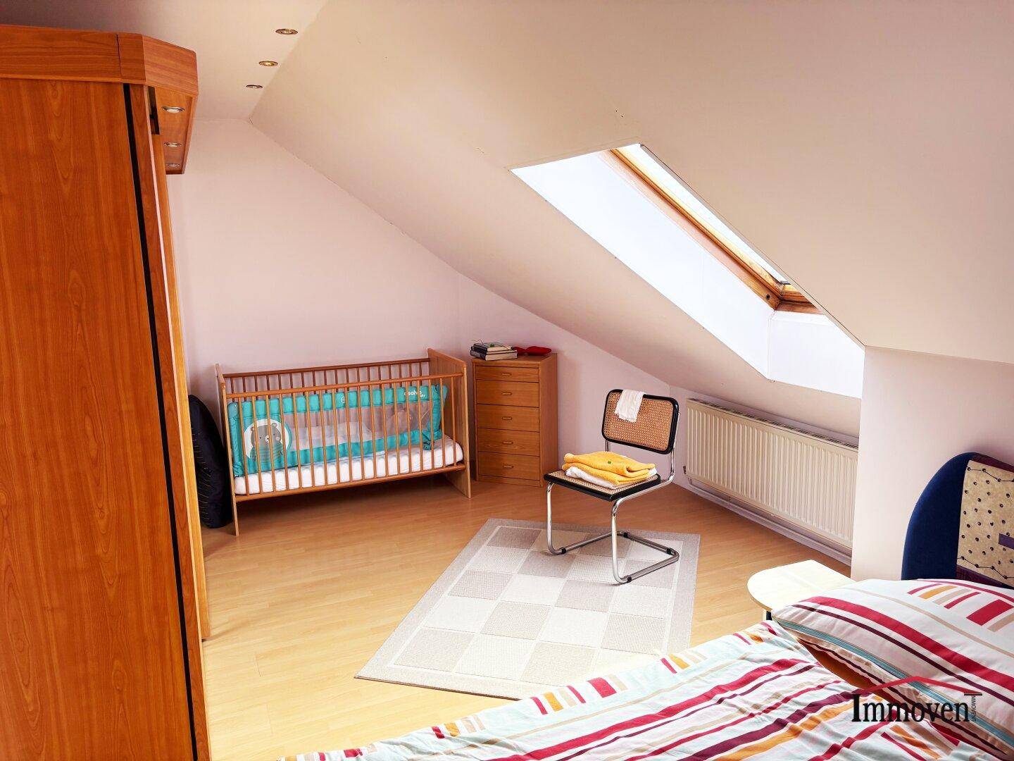 Helles Schlafzimmer im Dachgeschoss mit Babybett, Kleiderschrank und einem praktischen Dachfenster.