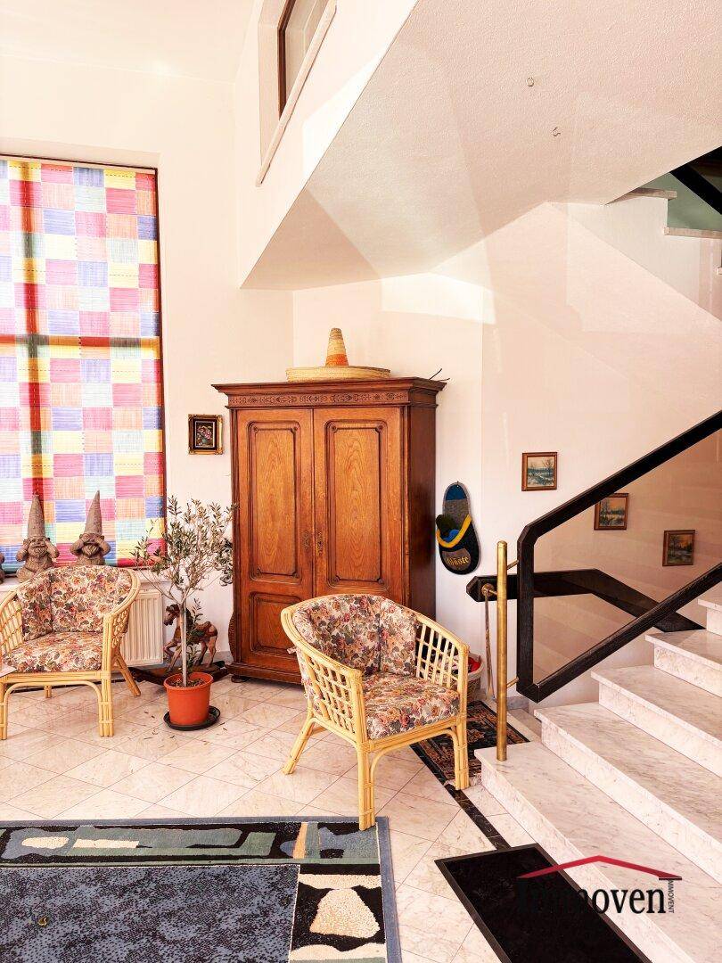 Geräumiger Flur mit Marmortreppe, Holzschrank und bunten Fensterrollos.