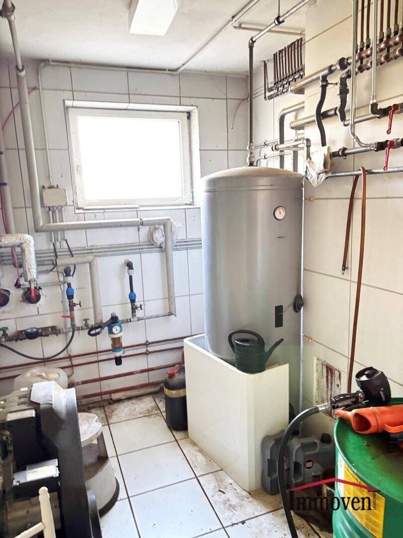 Heizungsraum mit großem Warmwasserspeicher, sichtbaren Rohren und gefliesten Wänden.