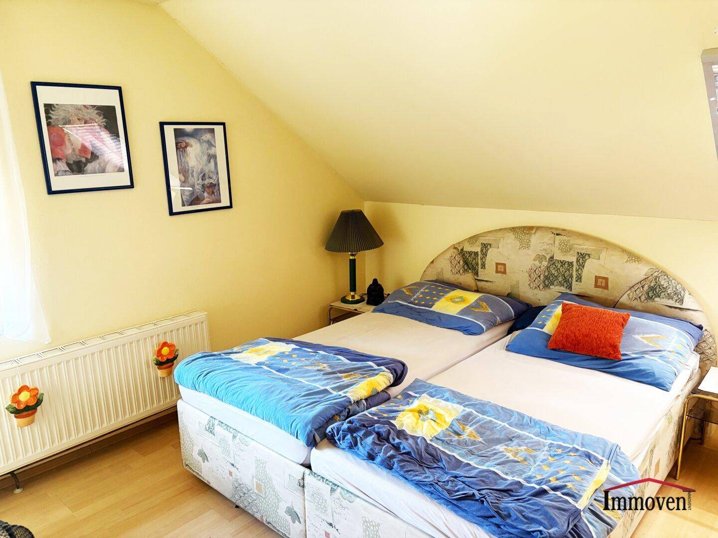 Schlafzimmer mit zwei Einzelbetten und Heizkörper, dekoriert mit Bildern an der Wand.