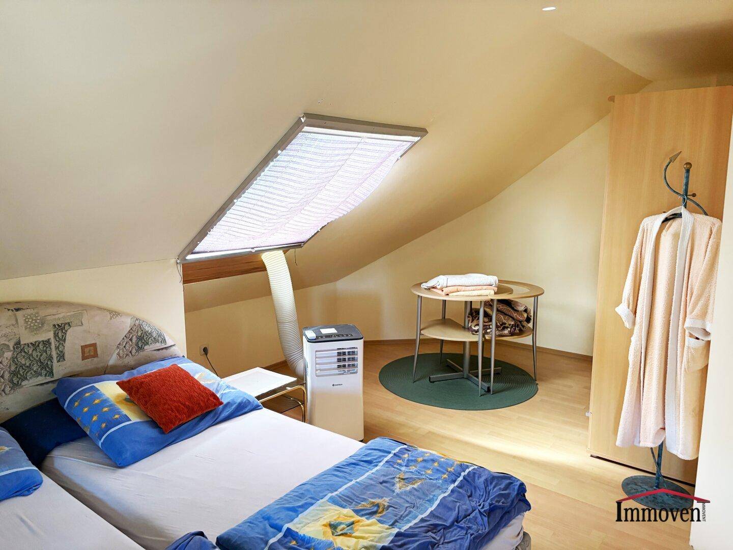 Schlafzimmer im Dachgeschoss mit zwei Einzelbetten, mobiler Klimaanlage und Dachfenster mit Jalousie.