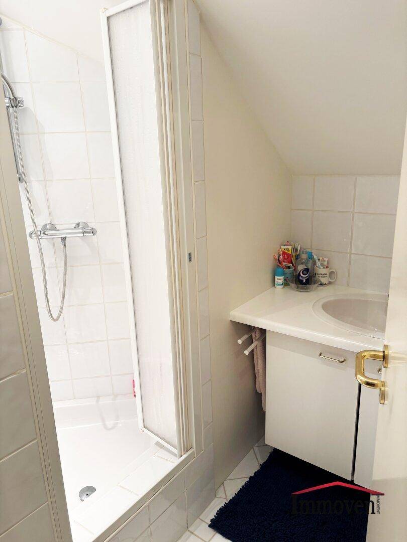 Kleines Badezimmer im Dachgeschoss mit Duschkabine, Waschbecken und schräger Decke.