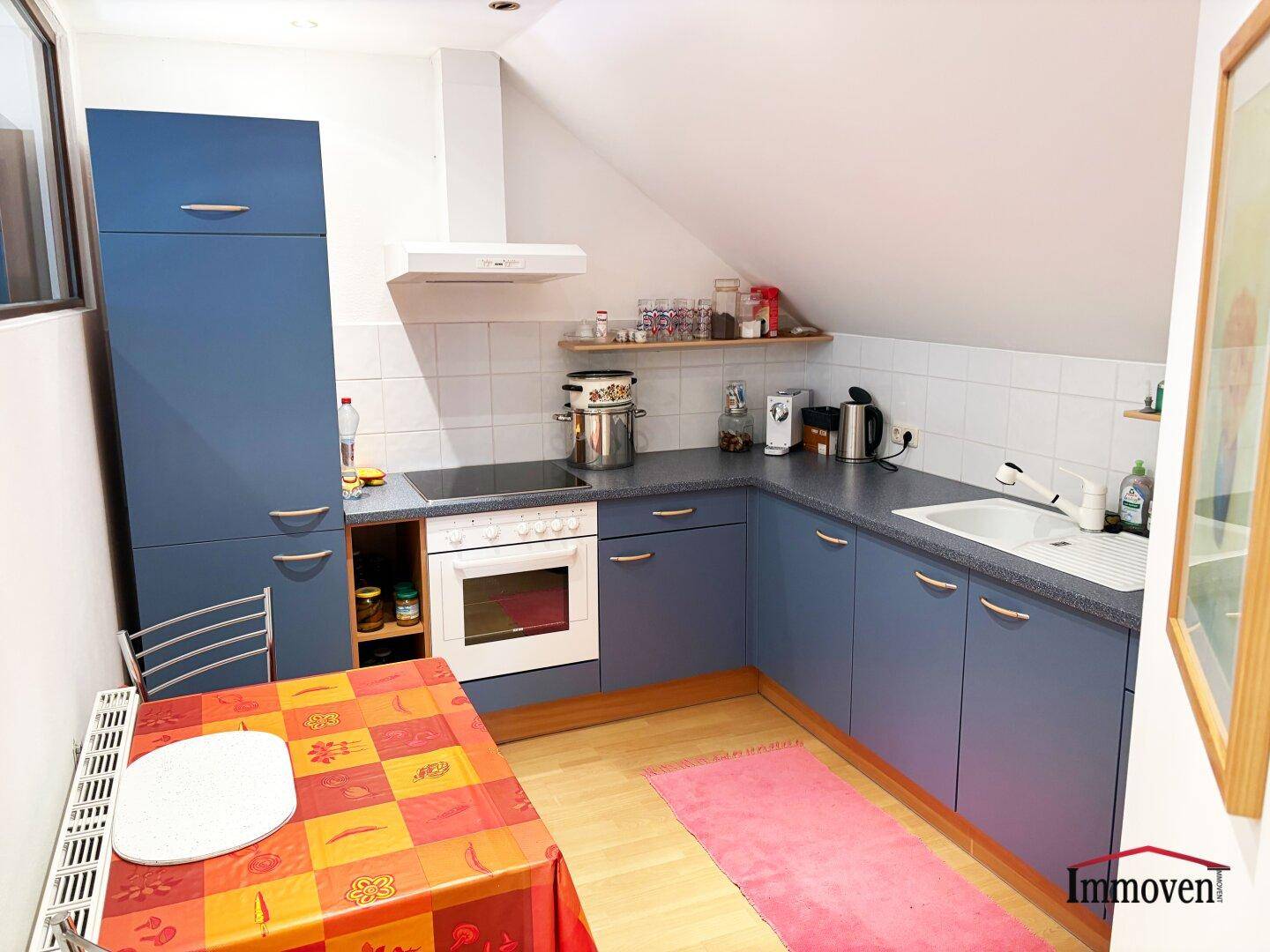 Dachgeschossküche mit blauen Einbauschränken, kleinem Esstisch und schräger Decke.