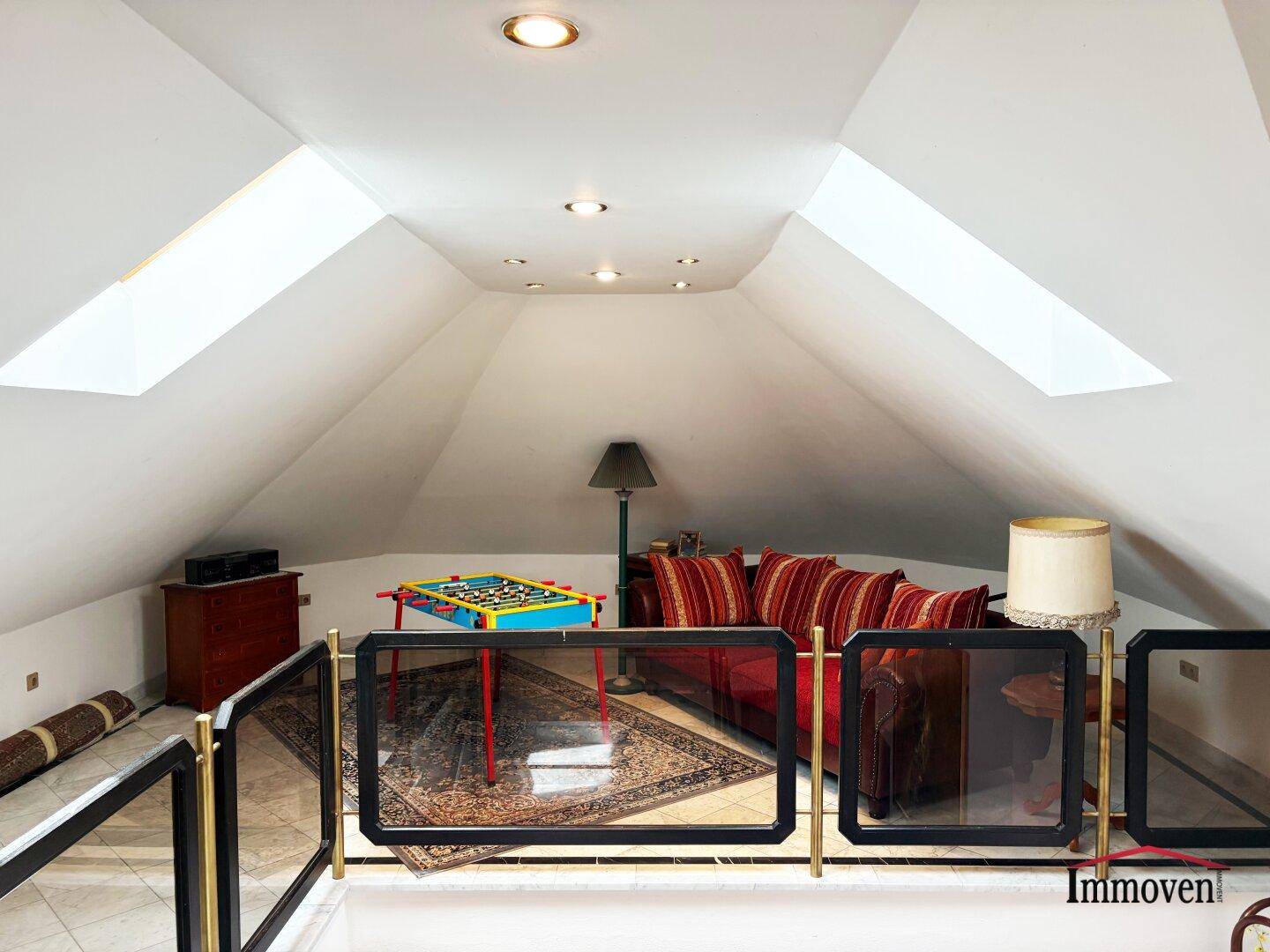 Offener Wohnbereich über dem Treppenhaus mit Sofa, Kicker und mehreren Dachfenstern.
