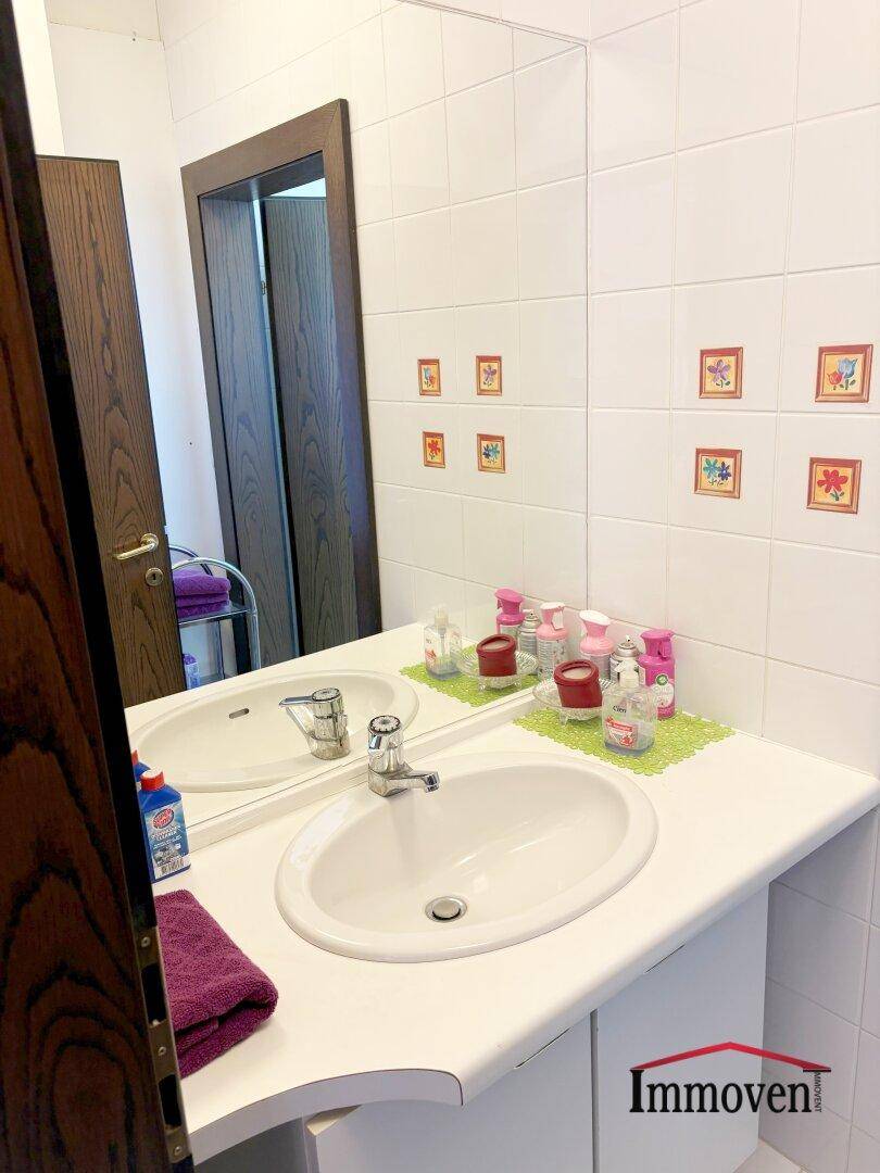 Badezimmer mit Einzelwaschbecken, großem Spiegel und weißen Fliesen mit dekorativen Akzenten.