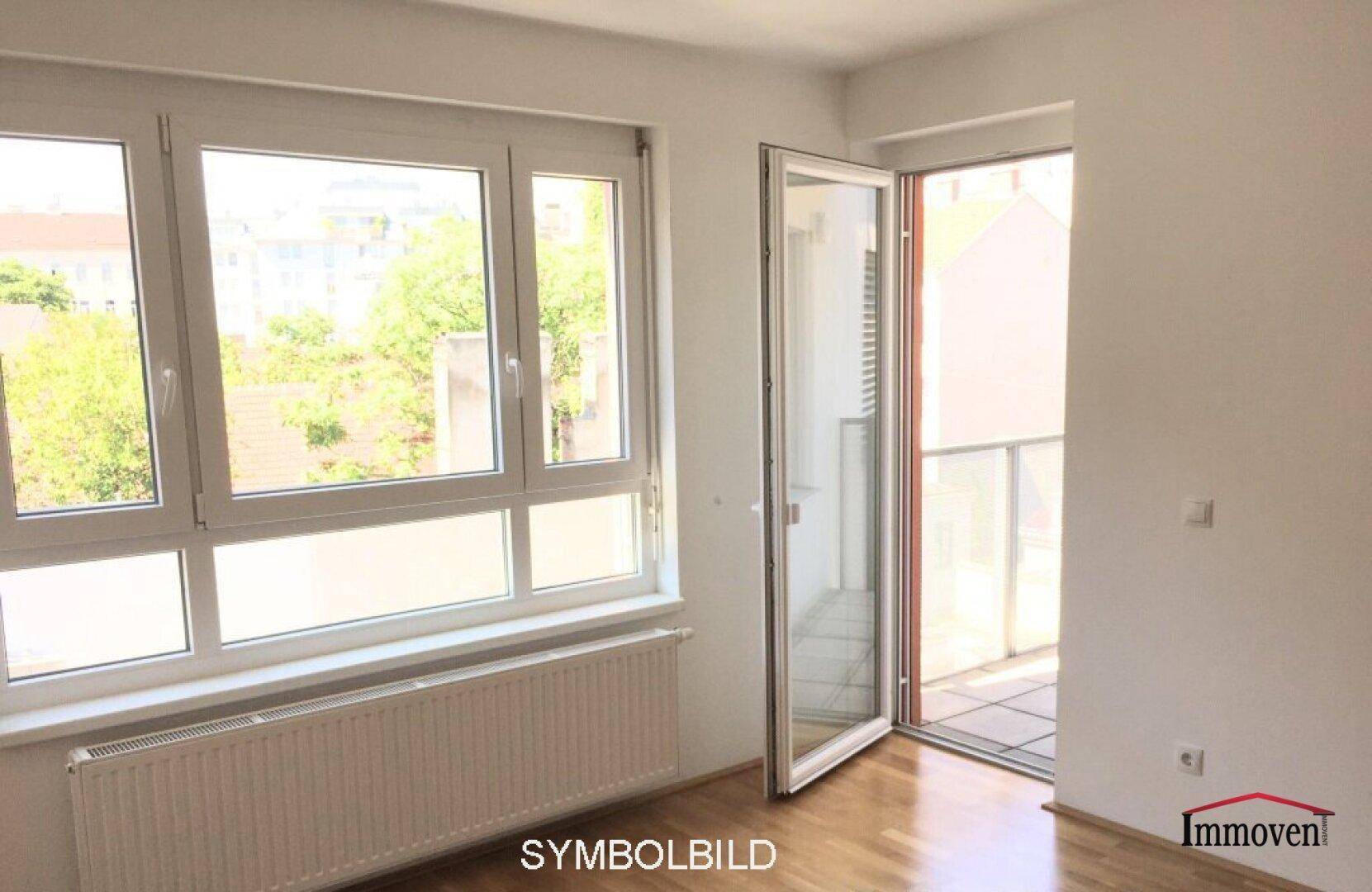 Heller Raum mit großen Fenstern, Holzboden und Zugang zu einem Balkon mit Blick ins Grüne.