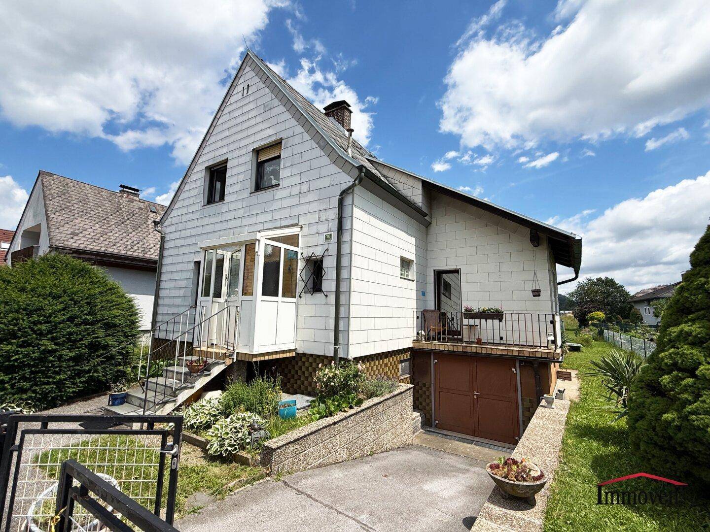 Weiß verputztes Einfamilienhaus mit Satteldach, Wintergarten und Garagenzufahrt.