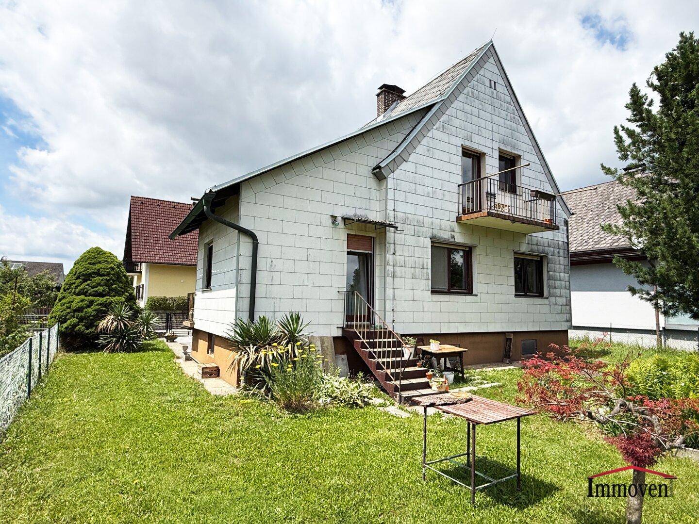 Weißes Einfamilienhaus mit Garten, Rasenfläche und einem kleinen Balkon.