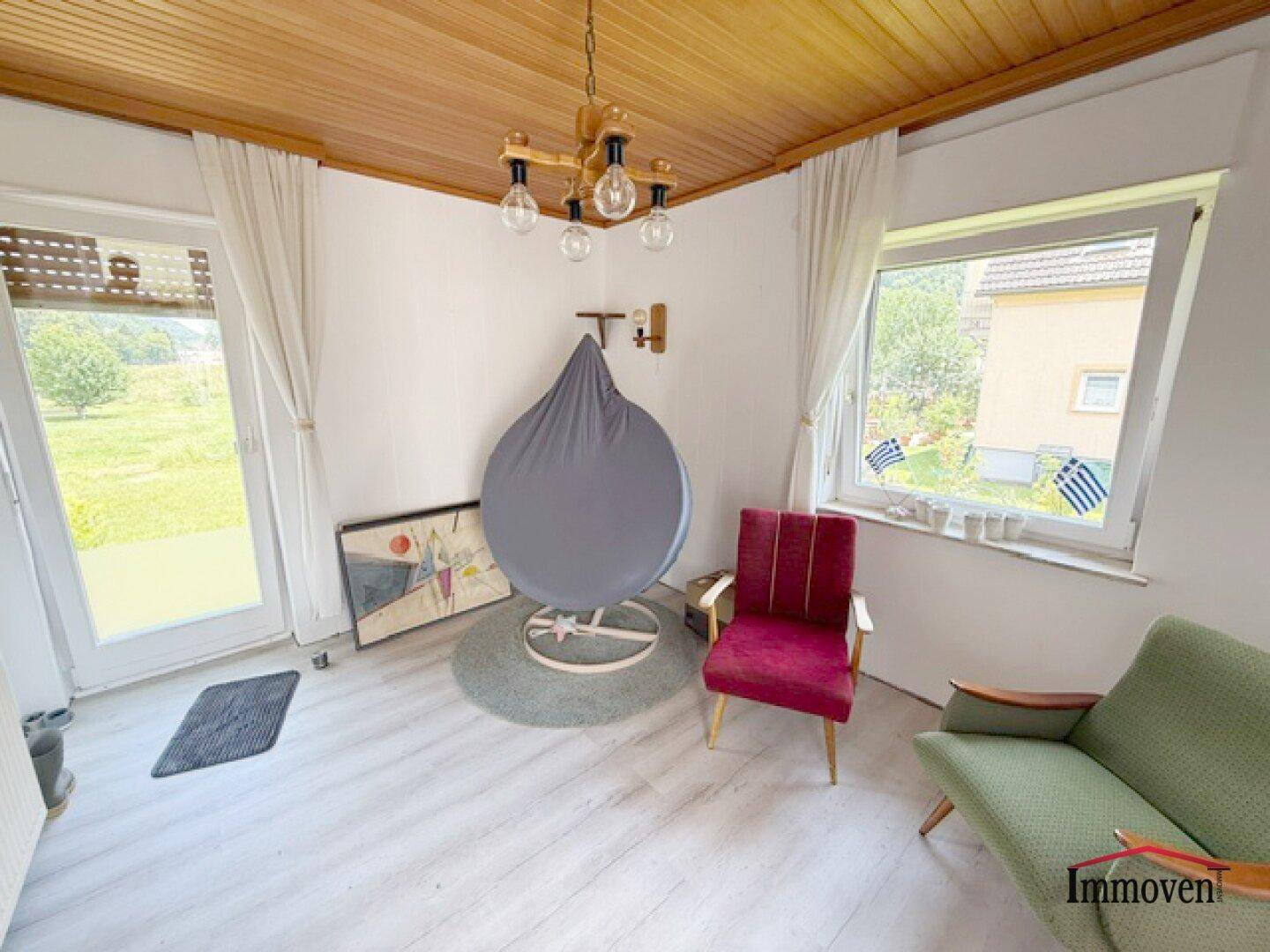 Heller Raum mit Holzdecke, großen Fenstern und einer Tür zum Gartenbereich.