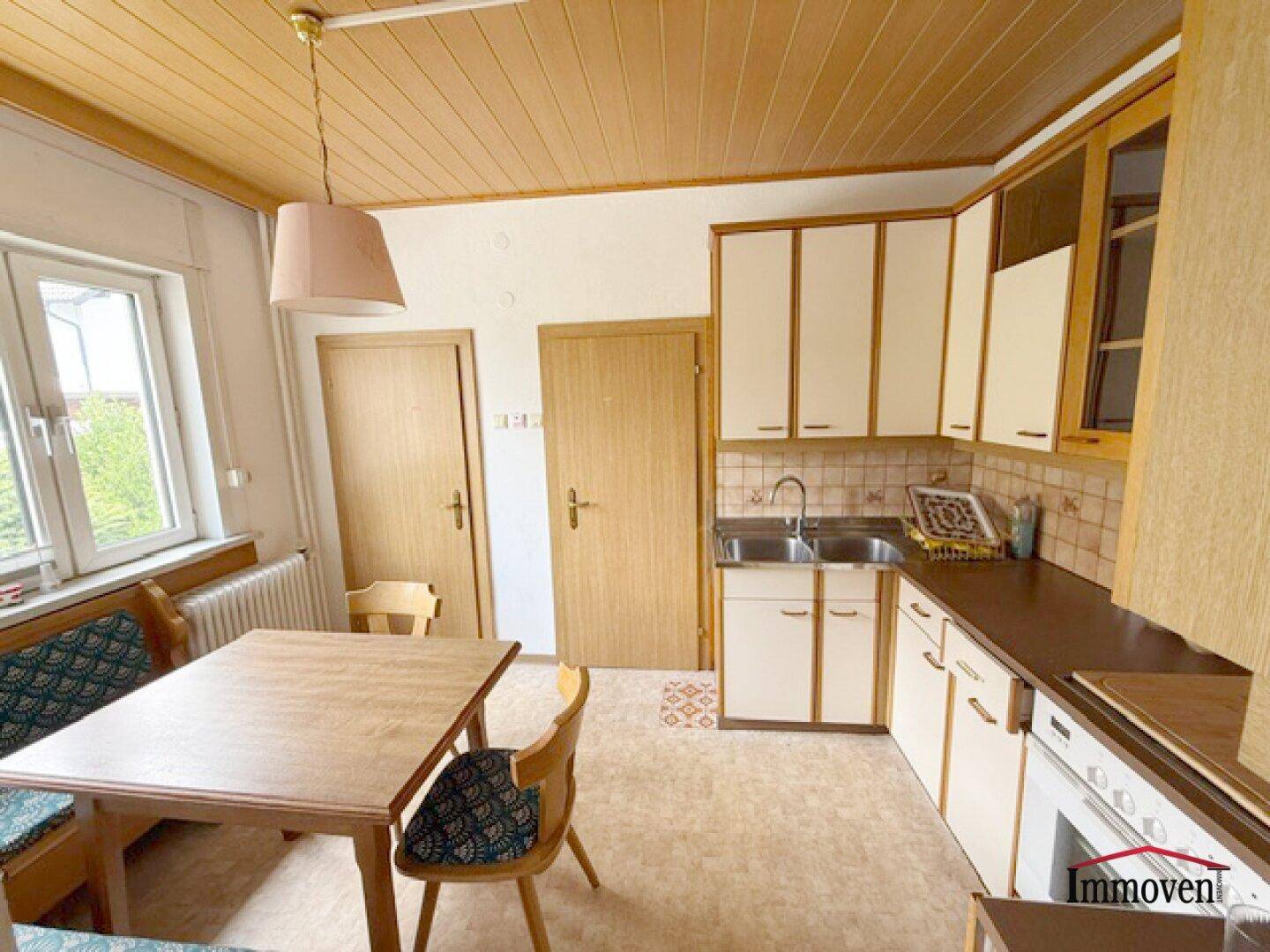 Helle Küche mit Holzdecke, Essbereich und Blick nach draußen durch ein Fenster.