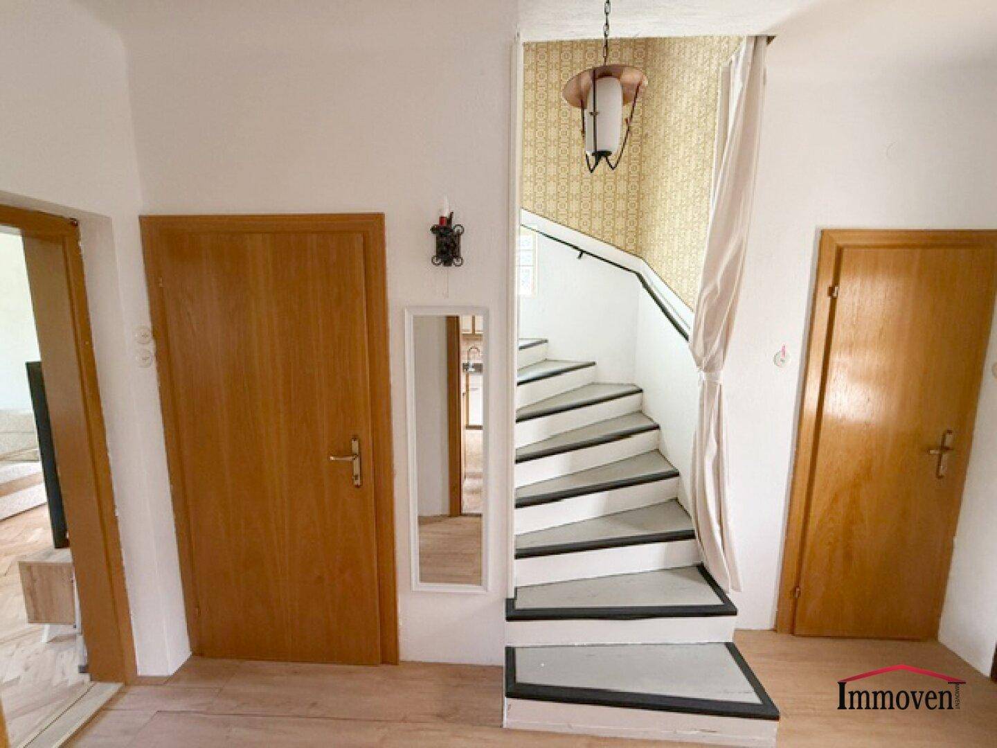 Eingangsbereich mit Holztreppe, Holztüren und einem Spiegel.