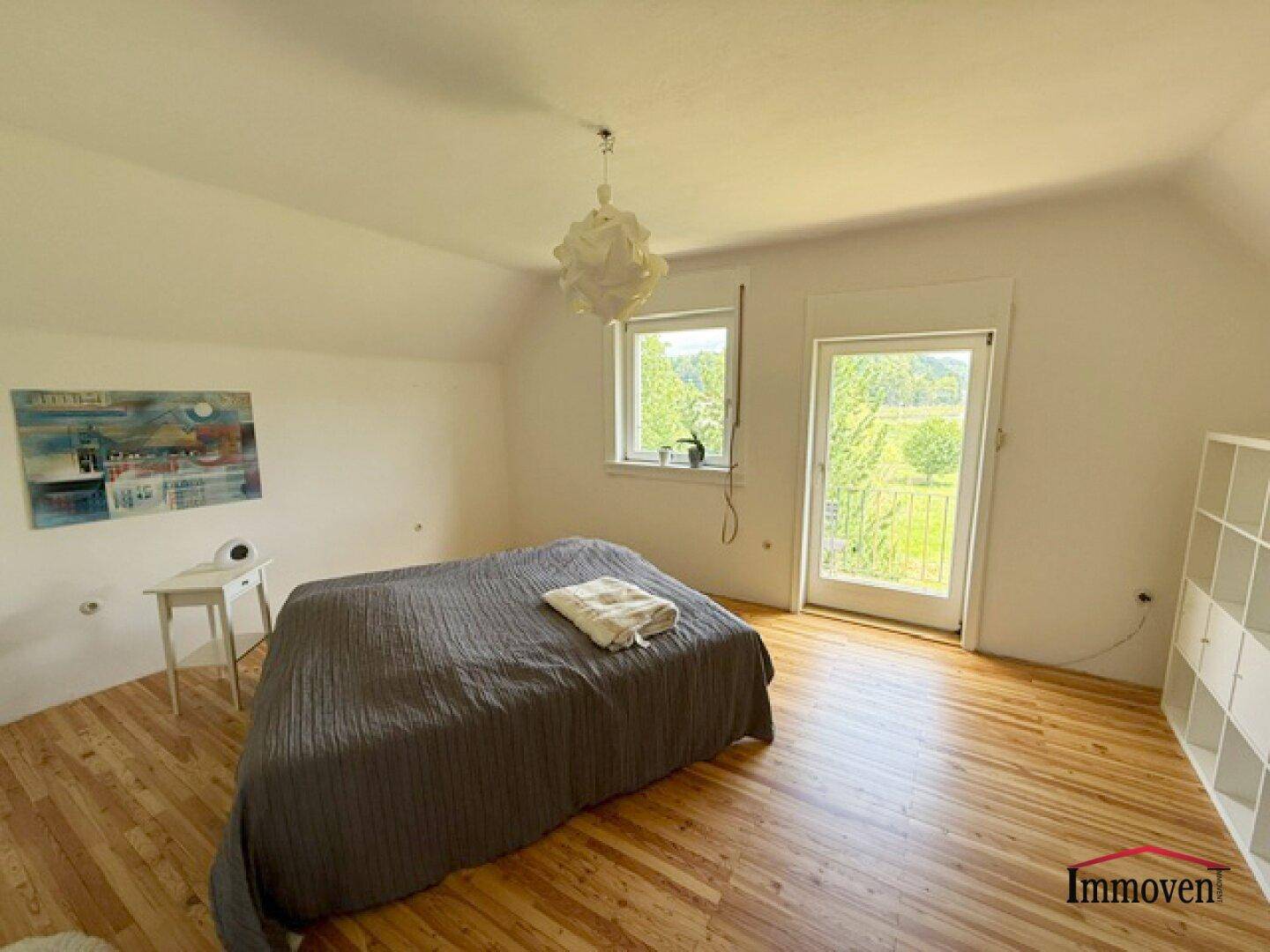 Helles Schlafzimmer mit Holzboden, Doppelbett und Zugang zu einem französischen Balkon.