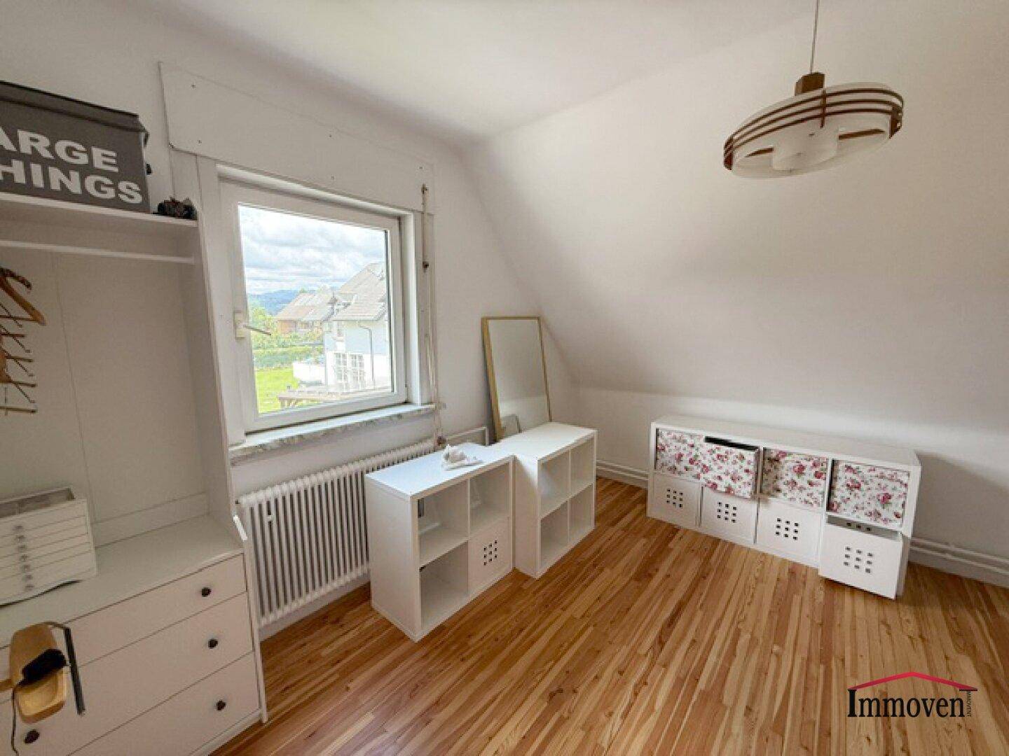 Schlafzimmer mit Holzboden, Fenster und Stauraumregalen unter einer Dachschräge.