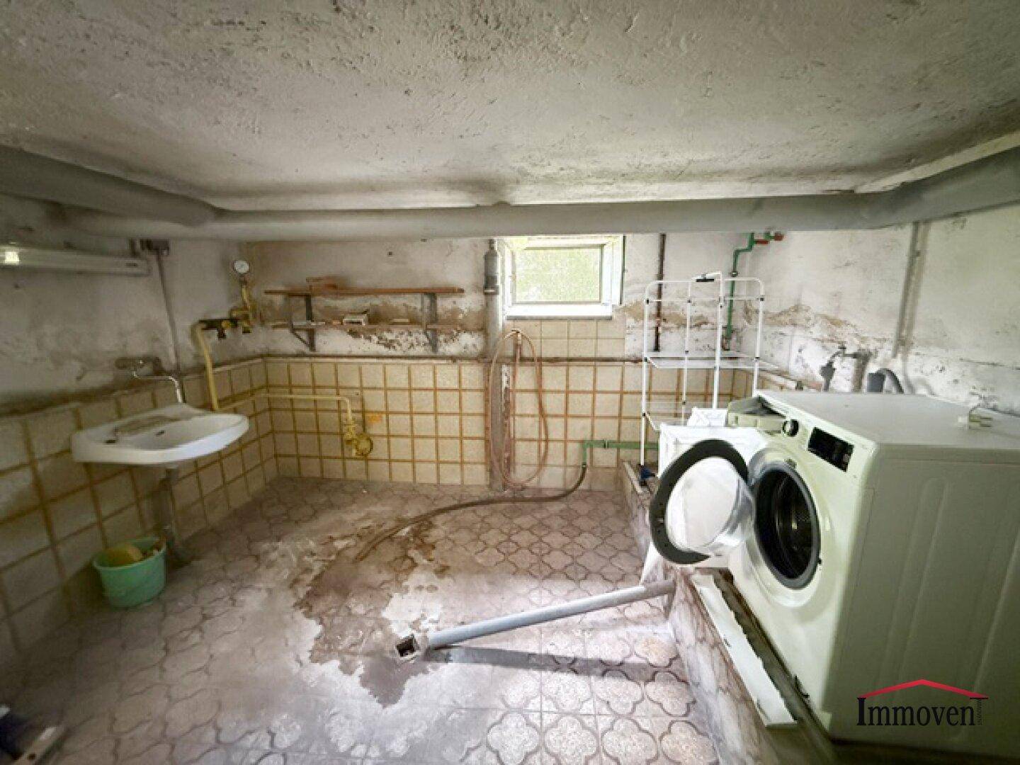 Waschküche im Keller mit Waschmaschine, Waschbecken und gefliesten Wänden.