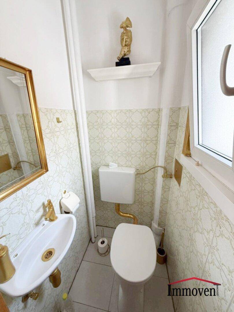 Kleines Gäste-WC mit Fenster, weißer Toilette und goldenen Armaturen.