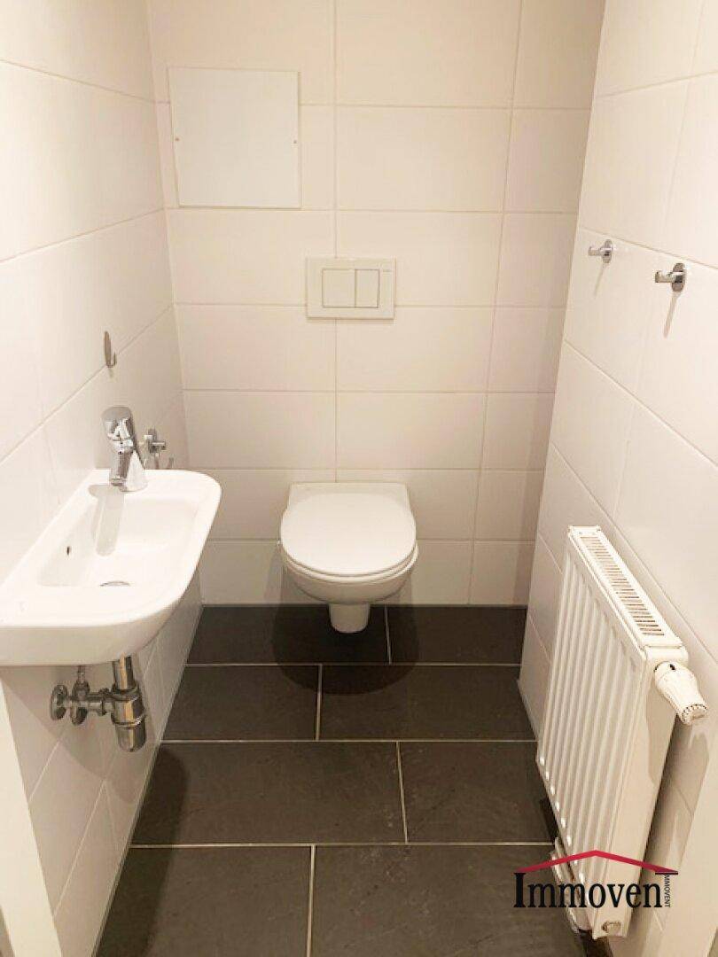 Separates Gäste-WC mit Wand-WC, kleinem Waschbecken und dunklem Fliesenboden.