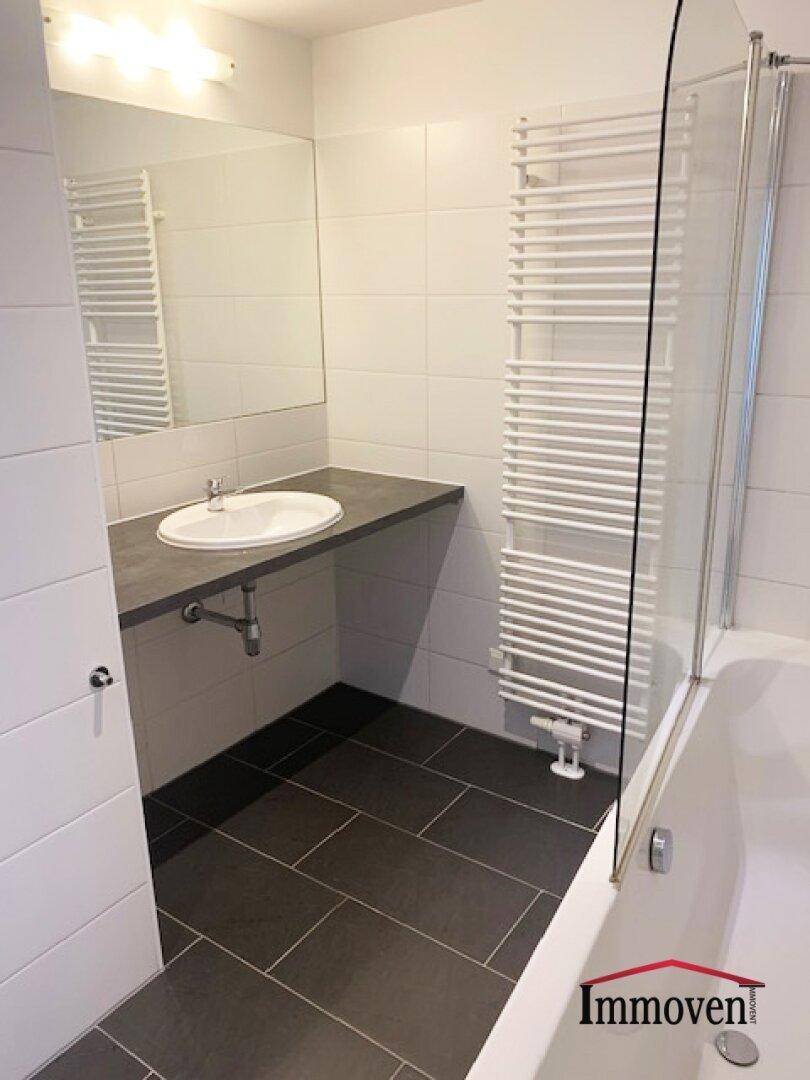 Modernes Badezimmer mit dunklen Fliesen, Einzelwaschbecken, Badewanne und beheiztem Handtuchhalter.