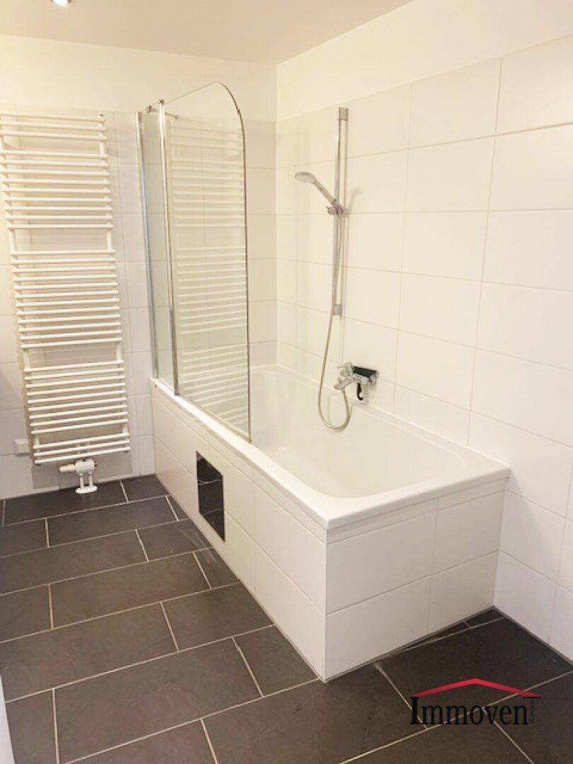 Geräumige Badewanne mit Duschabtrennung aus Glas und integrierter Brause in modernem Badezimmer.