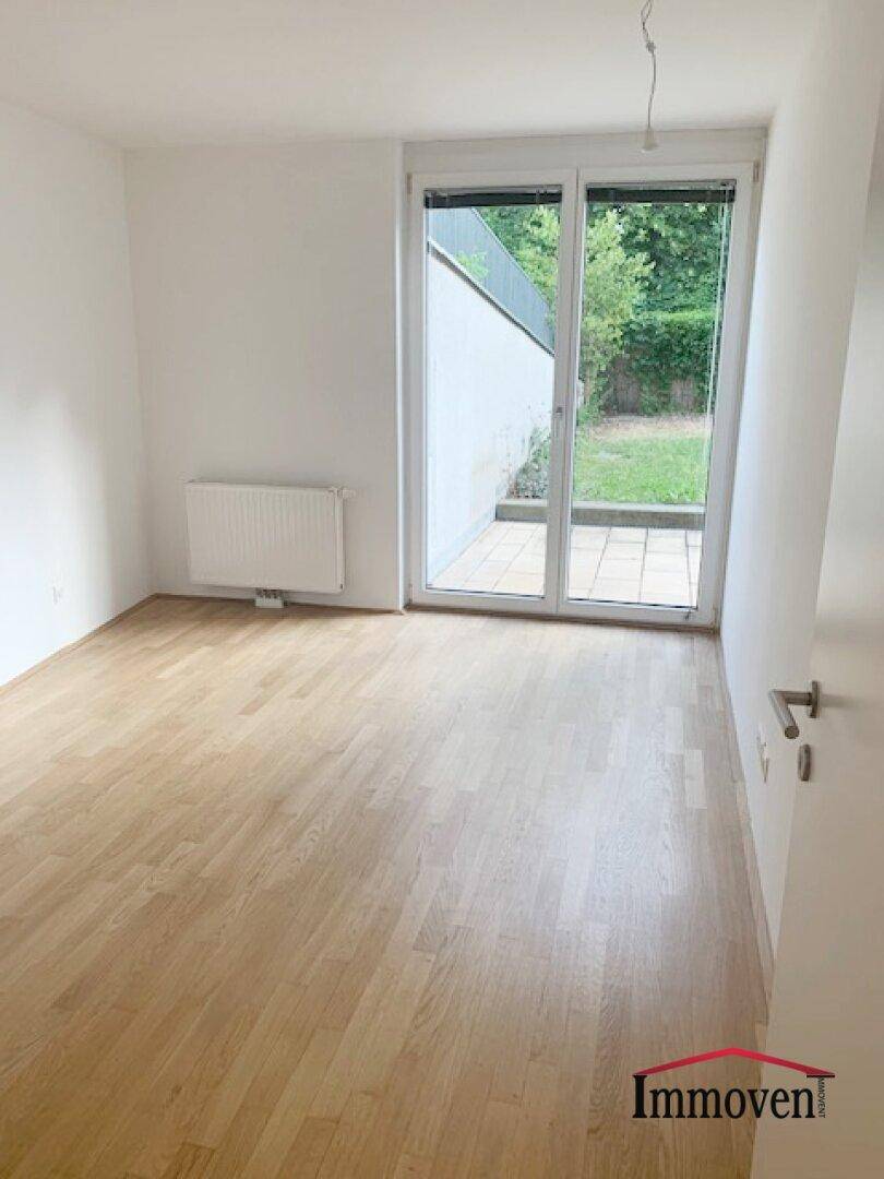 Helles Zimmer mit Parkettboden und direktem Zugang zu einer kleinen Terrasse und Grünfläche.