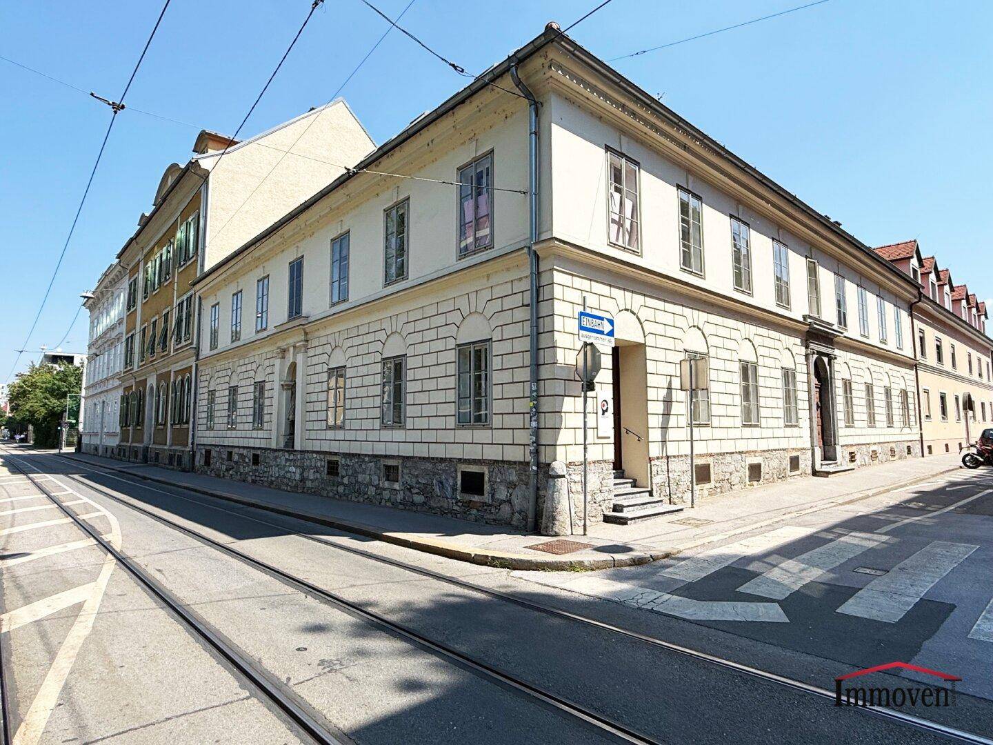 Historisches Eckgebäude an einer Straße mit Straßenbahnschienen, das eine klassische Architektur aufweist.