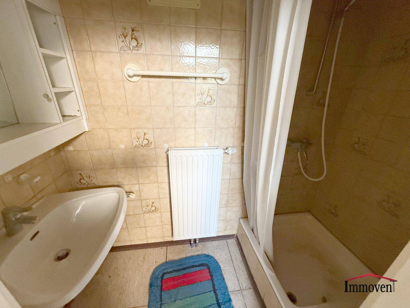 Badezimmer mit Badewanne, Waschbecken und beigen Fliesen, das eine funktionale Ausstattung bietet.
