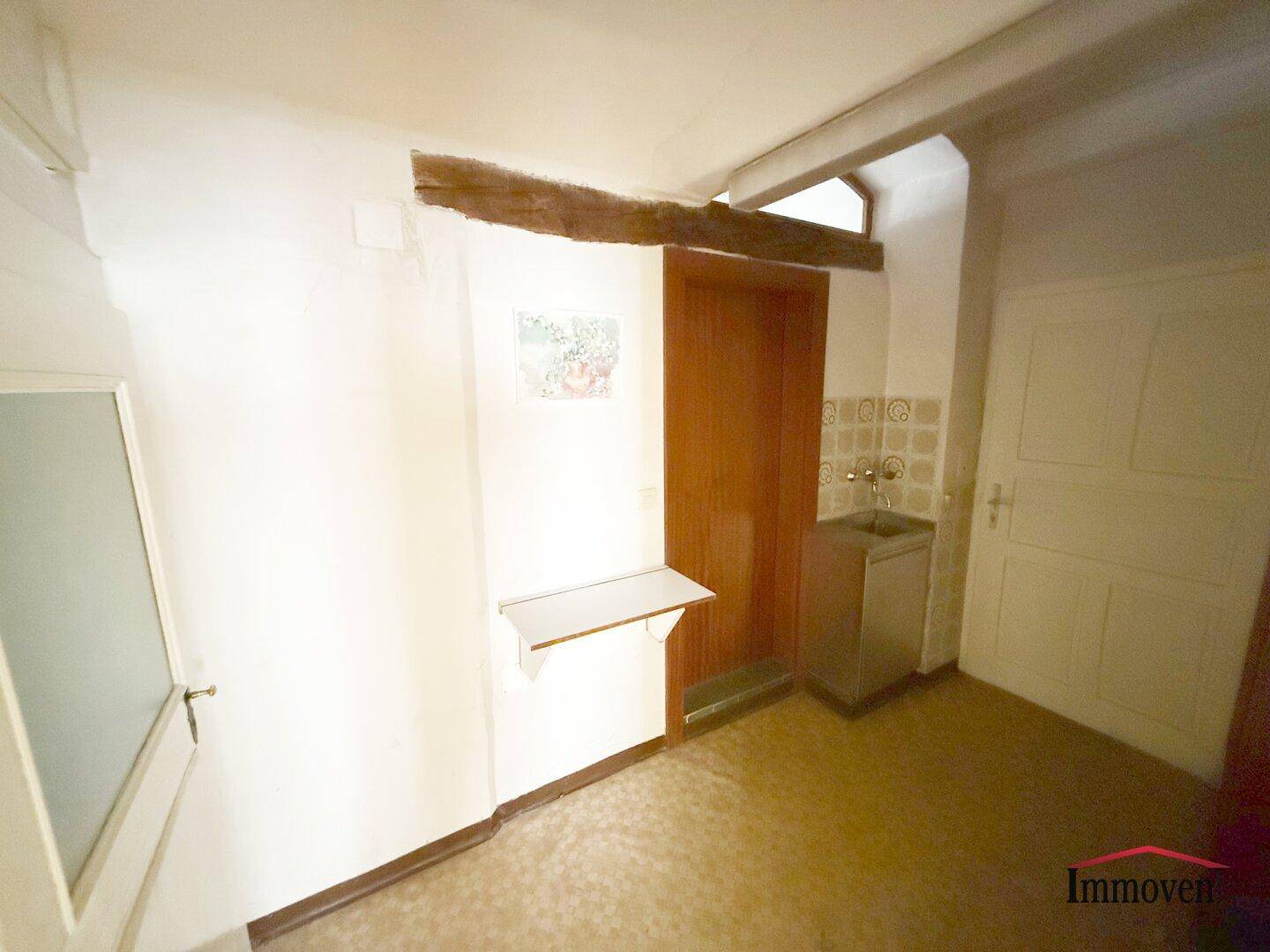 Kleiner Raum mit Waschbecken und Holzbalken, der als Abstell- oder Vorbereitungsbereich dienen könnte.