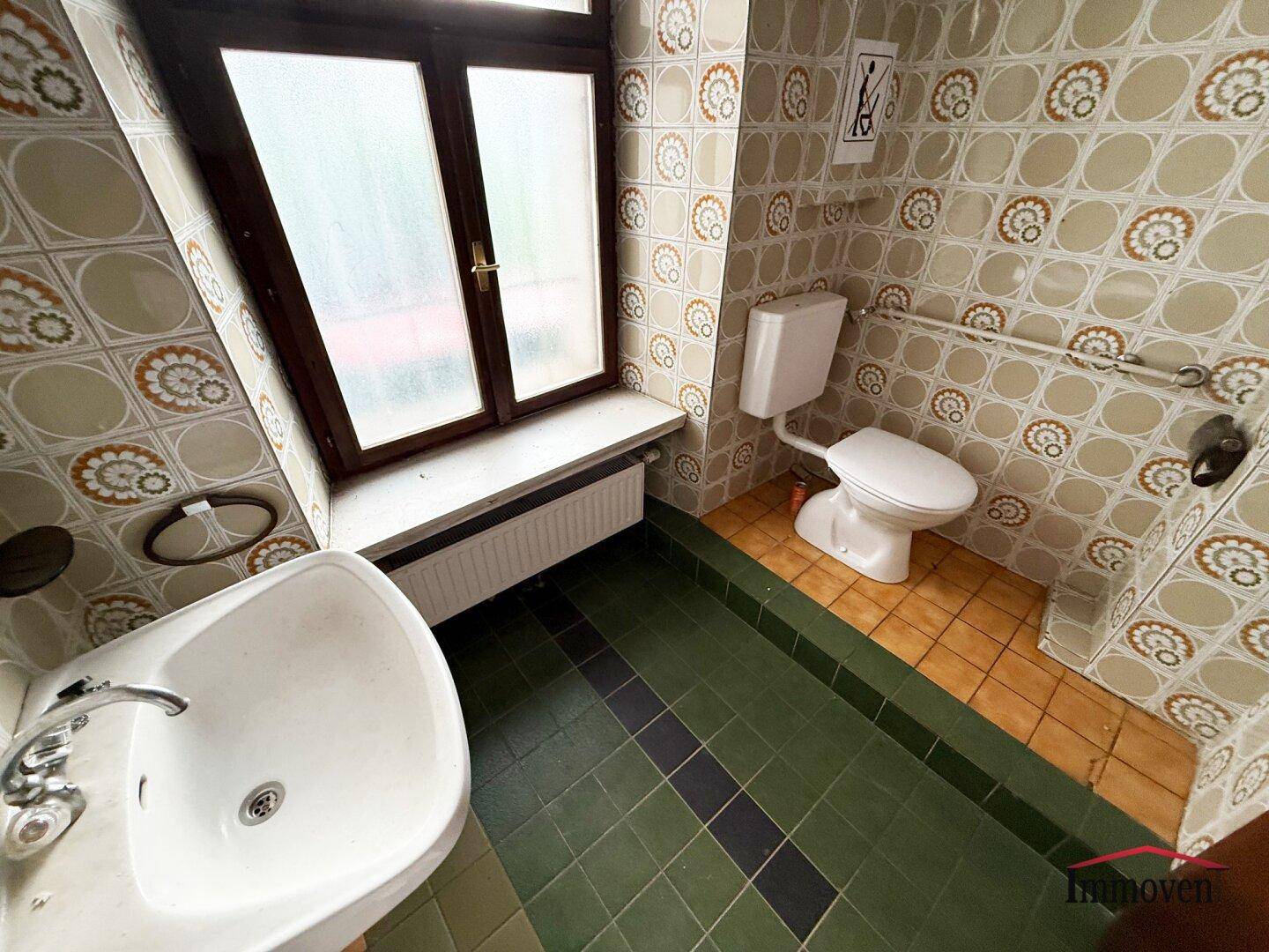 Badezimmer mit WC, Waschbecken und farbigen Fliesen, das ein Fenster für natürliche Belüftung hat.