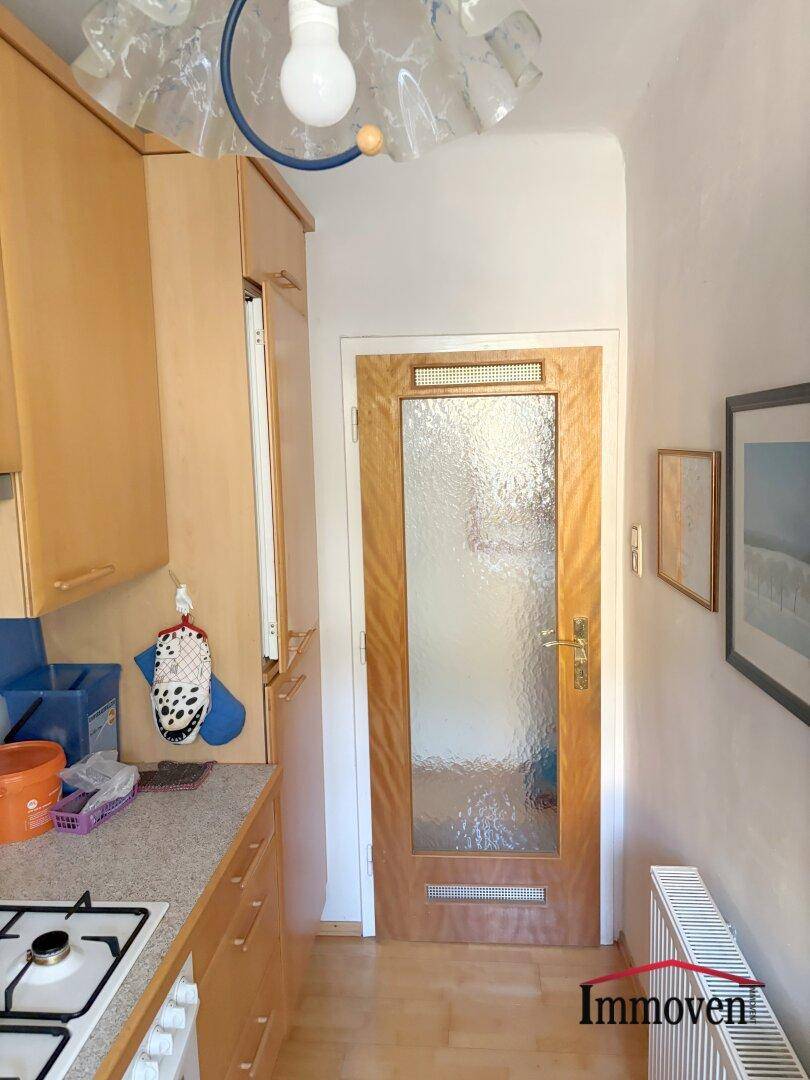 Küchenbereich mit Einbauschränken, Heizkörper und Holztür mit Glaseinsatz.