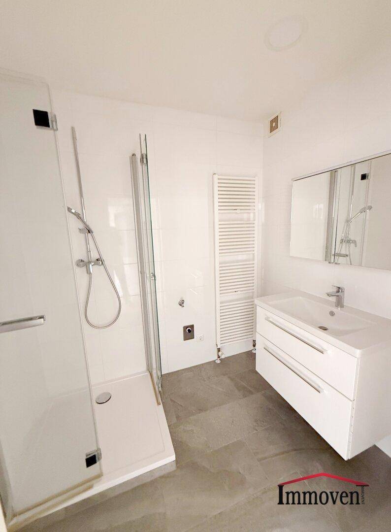 Modernes Badezimmer mit Duschkabine, Waschtisch, Spiegel und beheiztem Handtuchhalter.