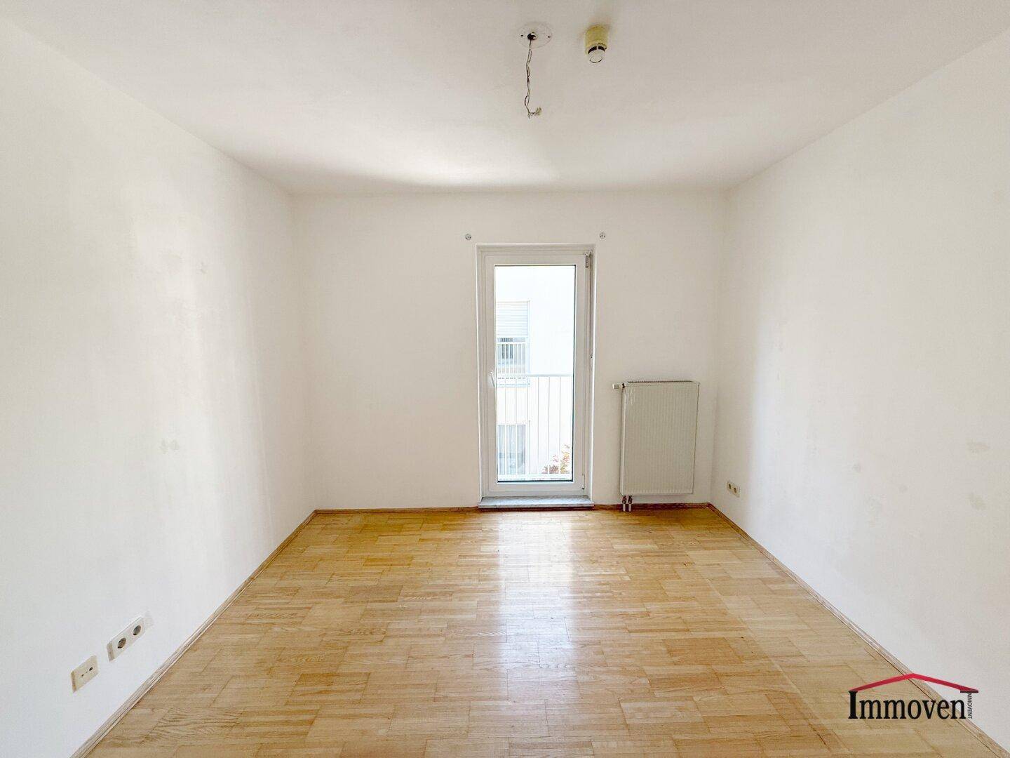 Helles Zimmer mit Parkettboden und Zugang zu einem französischen Balkon.