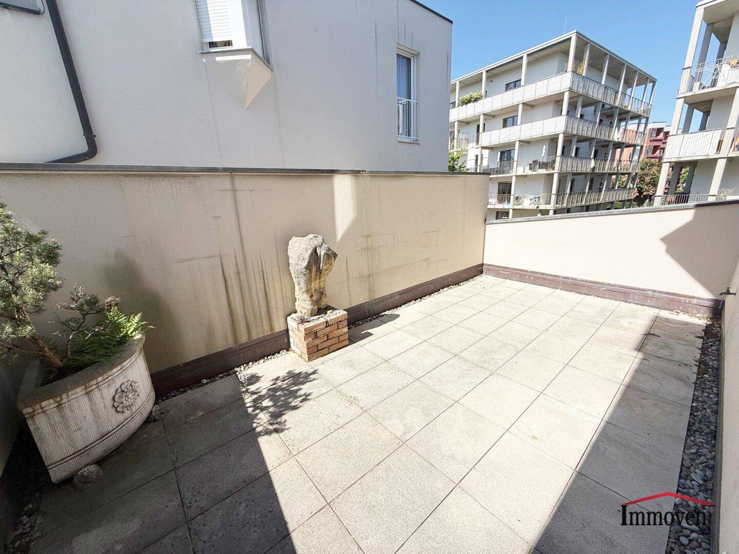 Geräumige, geflieste Terrasse mit hohen Mauern und Blick auf die umliegenden Gebäude.