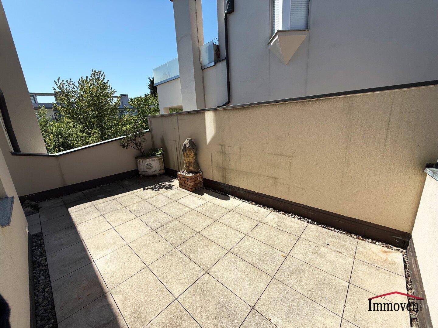 Sonniger Terrassenbereich mit Fliesenboden und einer kleinen Pflanze in einem Topf.
