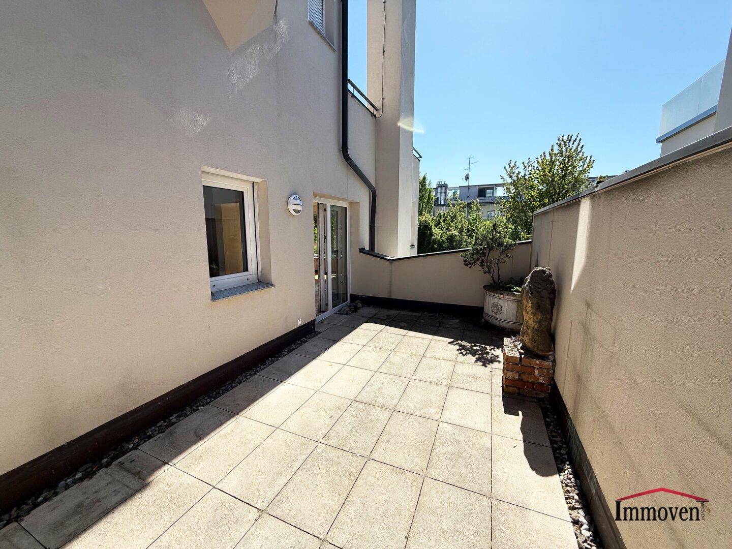 Lange Terrasse mit Fliesenboden, Zugang zum Gebäude und Blick auf die Nachbarschaft.