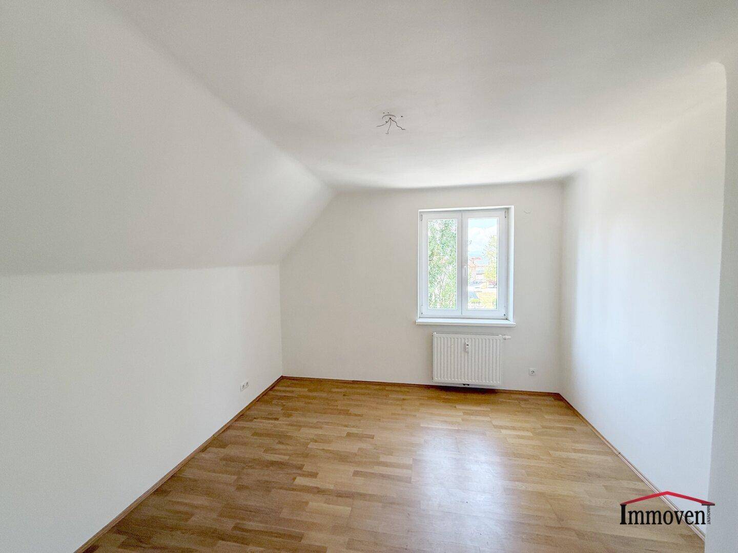 Geräumiges Schlafzimmer mit Dachschräge, hellem Parkettboden und einem Fenster.