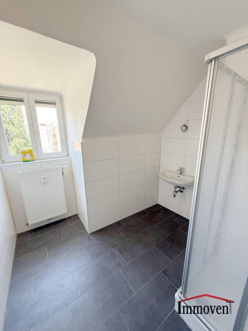Modernes Badezimmer mit Dusche, Waschbecken, dunklen Fliesen und Dachschräge.