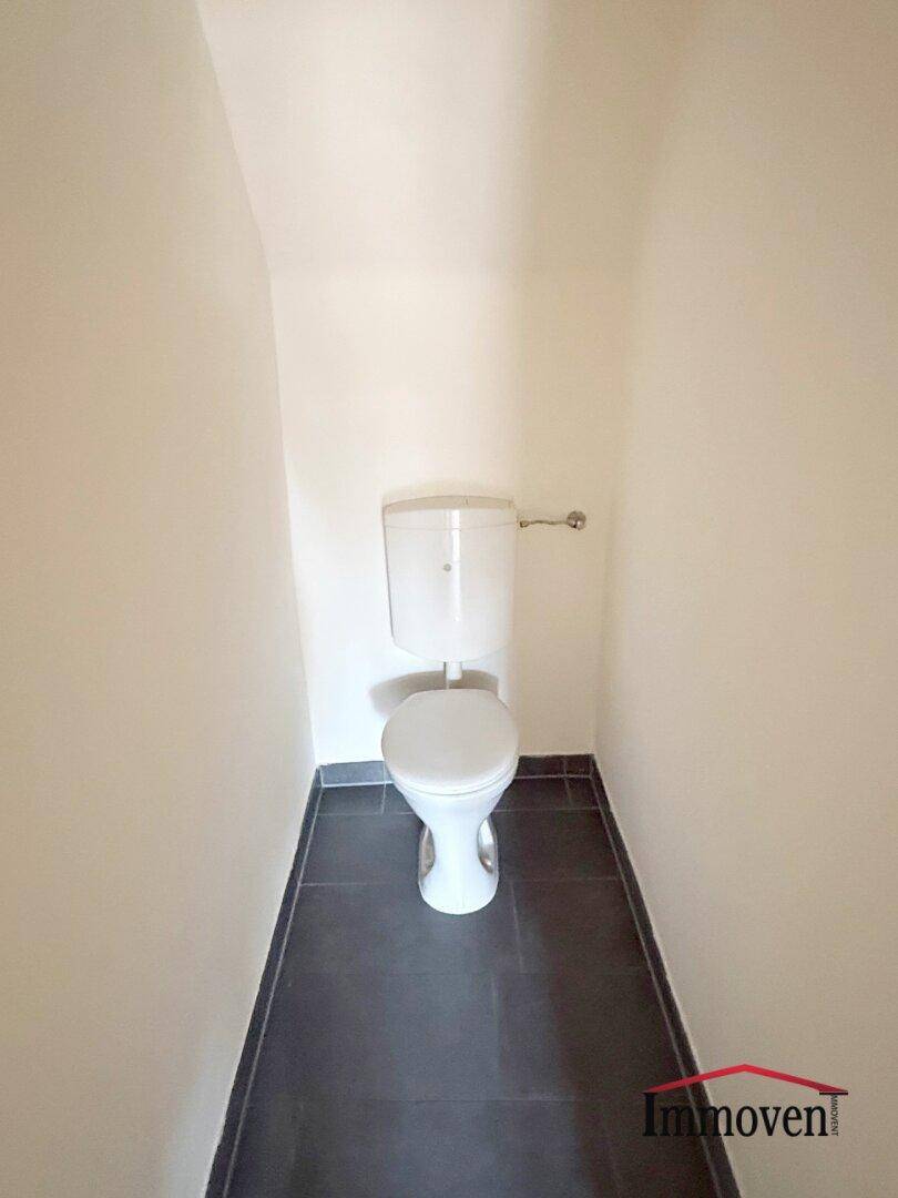 Separates WC mit Toilette und dunklen Bodenfliesen, in einem schlichten Design gehalten.