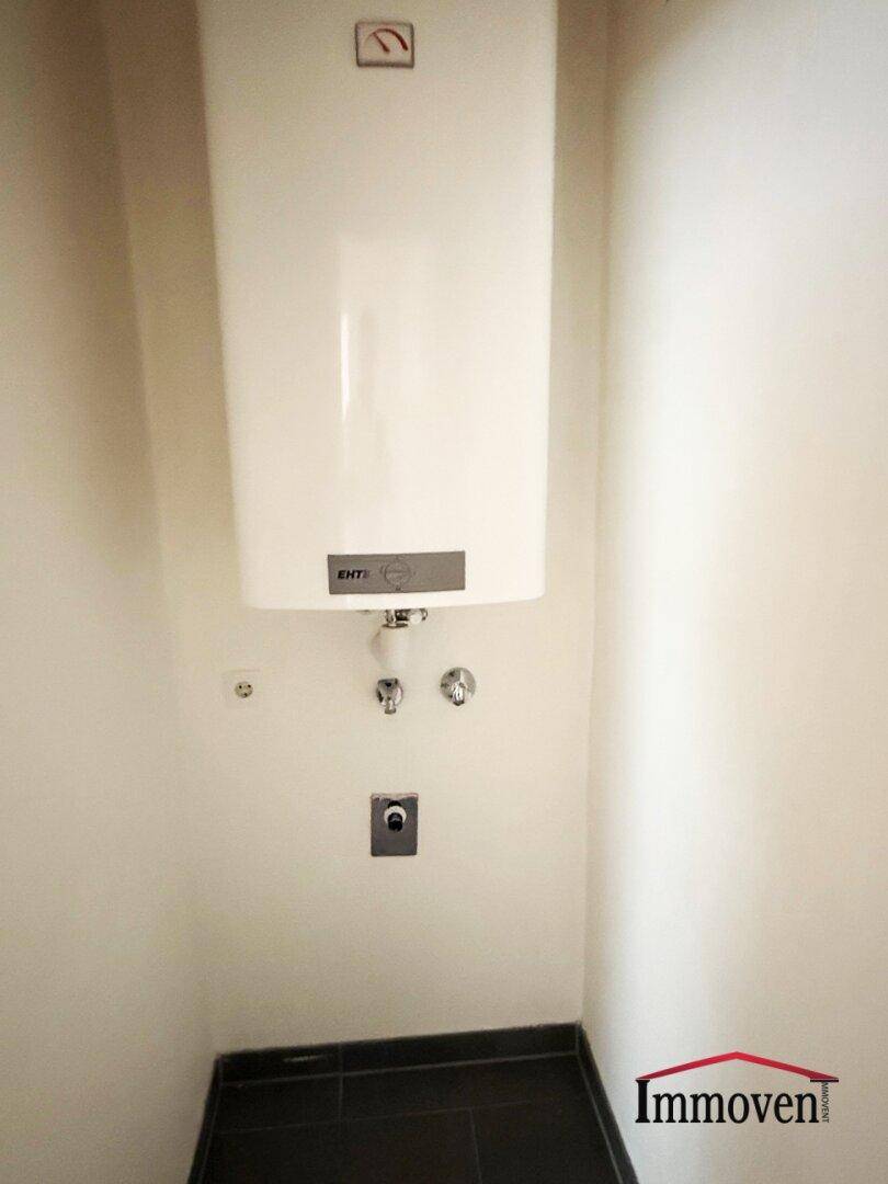 Kleiner Raum mit Warmwasserbereiter und dunklen Bodenfliesen, ideal als Abstellraum.