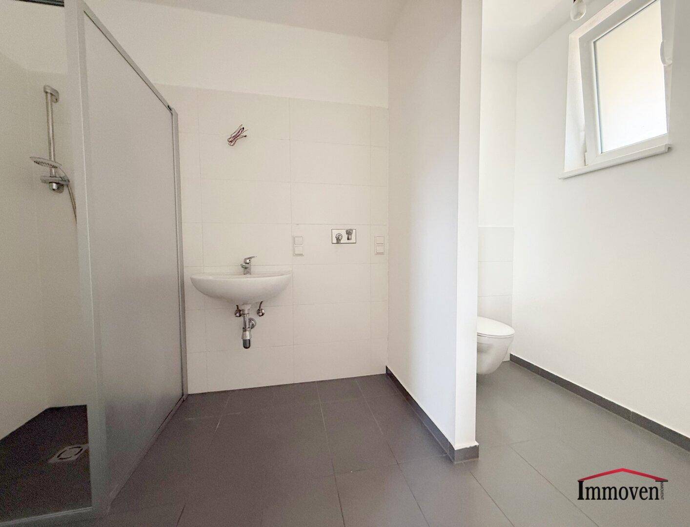 Modernes Badezimmer mit Dusche, WC, Waschbecken, Fliesenboden und Fenster.