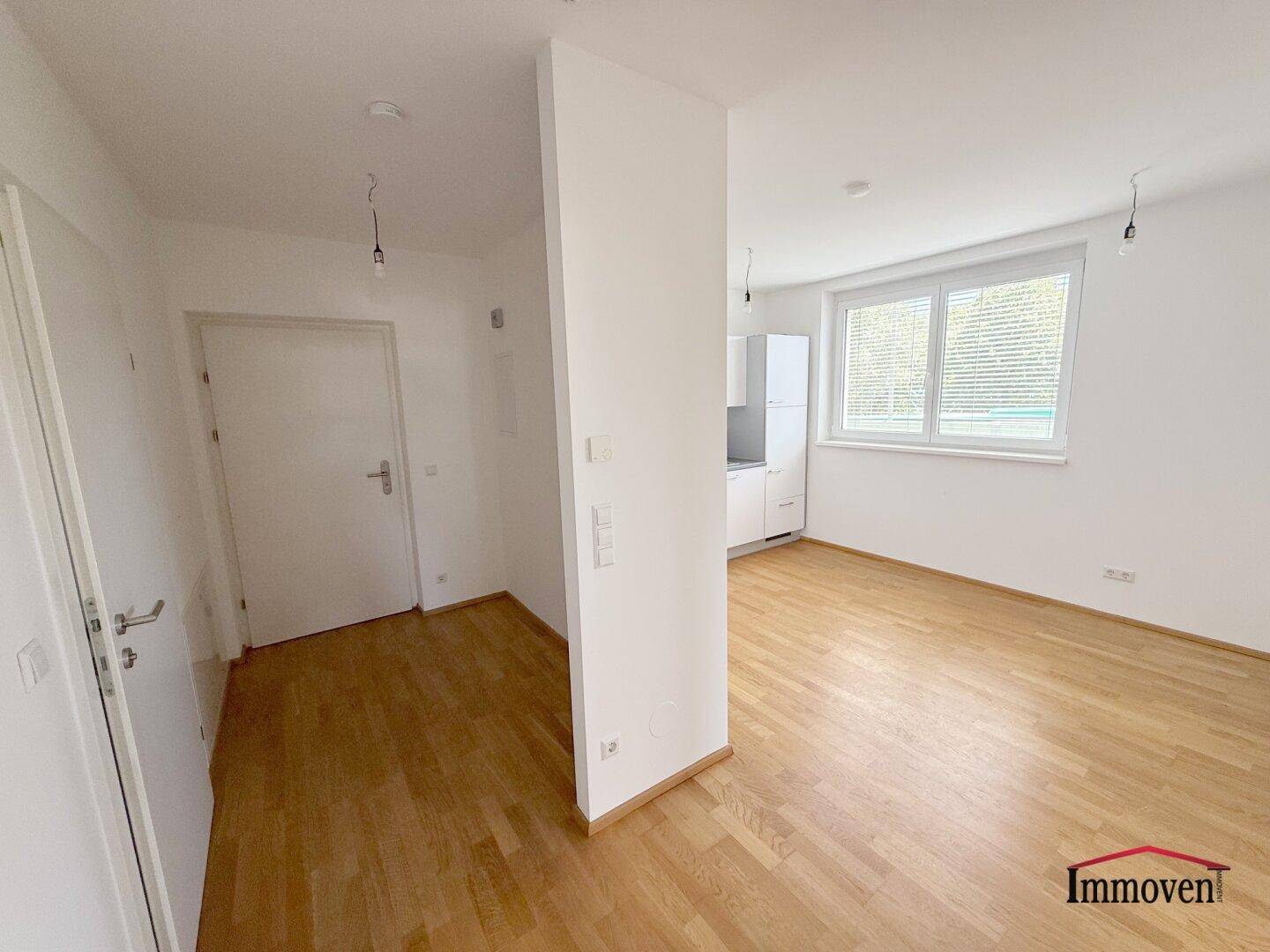 Flur mit Holzboden, der in einen hellen Raum mit Küchenzeile führt.