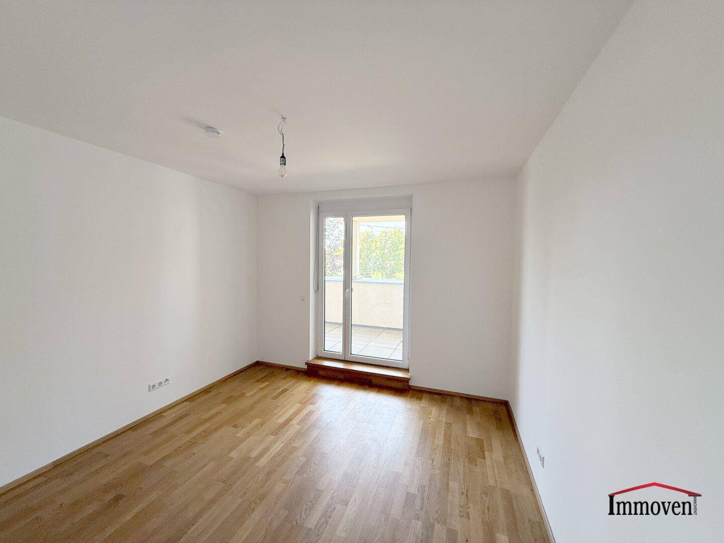 Leeres Zimmer mit Holzboden und direktem Zugang zu einem Balkon.