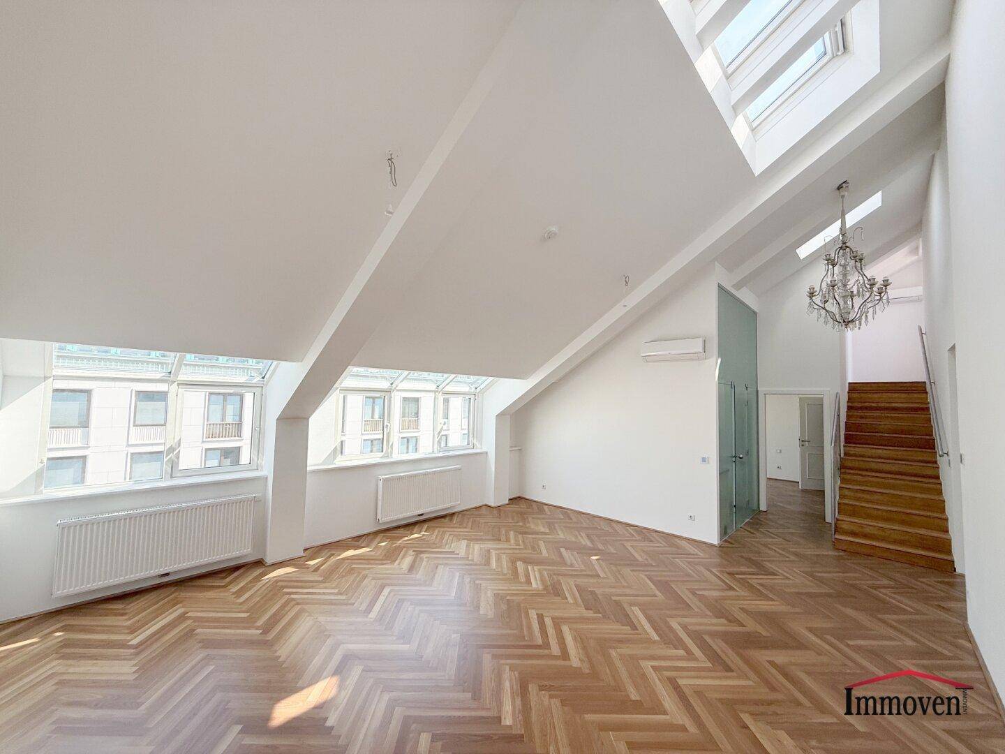 Helles Dachgeschoss-Wohnzimmer mit elegantem Fischgrätparkett, hohen Decken und großen Dachfenstern.