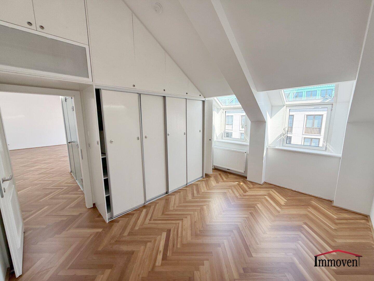 Schlafzimmer mit großen Einbauschränken, Fischgrätparkett und viel Tageslicht durch Dachfenster.