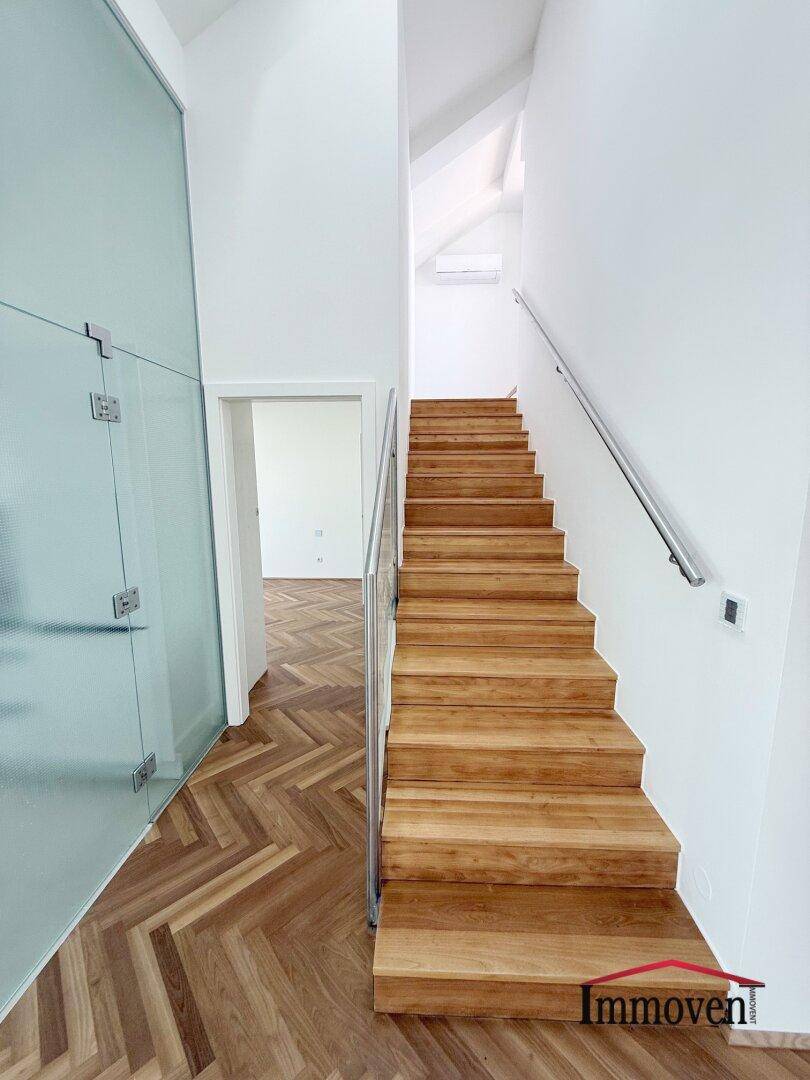 Treppenaufgang mit Holzstufen, Edelstahlgeländer und Glasabtrennung im Dachgeschoss.