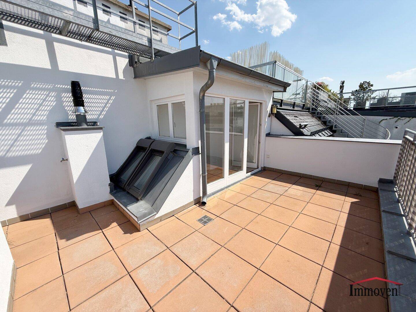 Sonniger Terrassenbereich mit Fliesenboden und Blick auf die umliegenden Dächer.