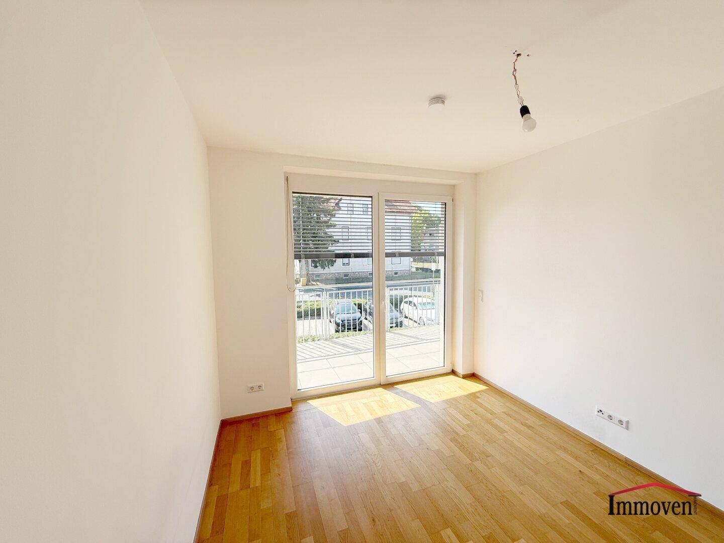 Lichtdurchflutetes Zimmer mit Holzboden und direktem Zugang zum Balkon, ideal für helle Wohnkonzepte.