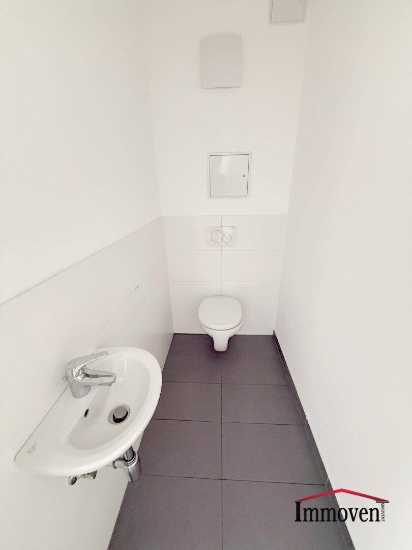 Separates Gäste-WC mit wandhängender Toilette und kleinem Handwaschbecken, modern gefliest.